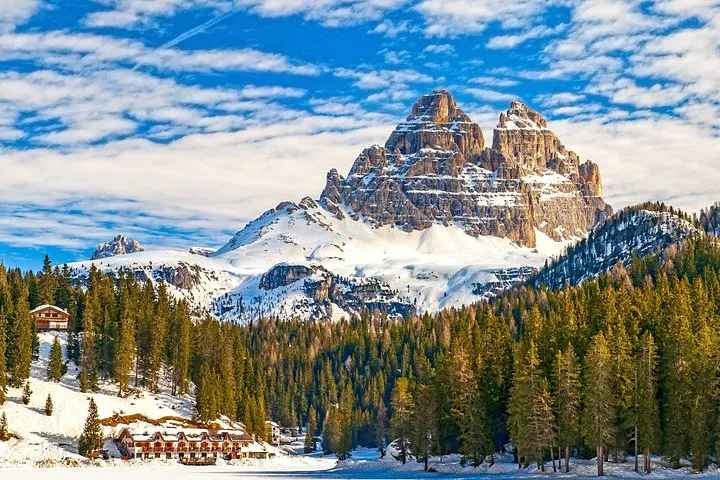 The snow-covered Three Peaks of Lavaredo above a winter forest and a lone refuge